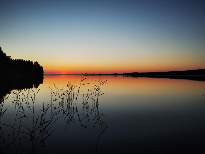 Auringonlasku ja peilityyni järvi Rääkkylässä kesäkuussa 2022.