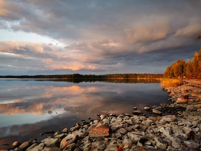 Pilviä ja ilta-auringon valoa järven rannalla.