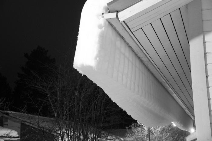 Märkä lumi roikkuu talon katolta. 